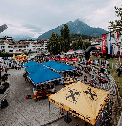 Belebter Platz in Bergen mit Pavillons und Menschen. Hintergrund: Berge und Wolken.