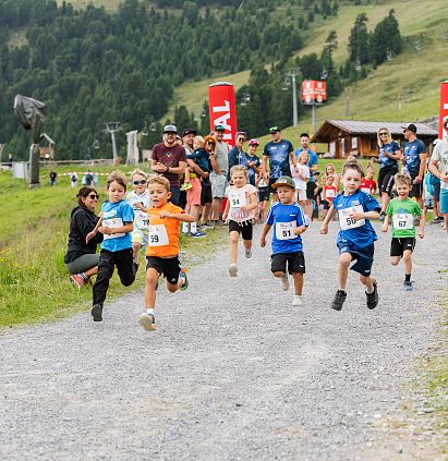 Kinder nehmen an einem Laufwettbewerb auf einem Waldweg teil, während Zuschauer am Rand zusehen.
