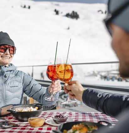Ein Paar stößt auf der Terrasse einer Skihütte im Skigebiet Hochzeiger mit zwei Aperol Spitz an.