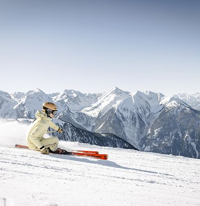 Skifahrerin auf sonniger Piste im Skigebiet Hochzeiger im Pitztal vor atemberaubender Bergkulisse.