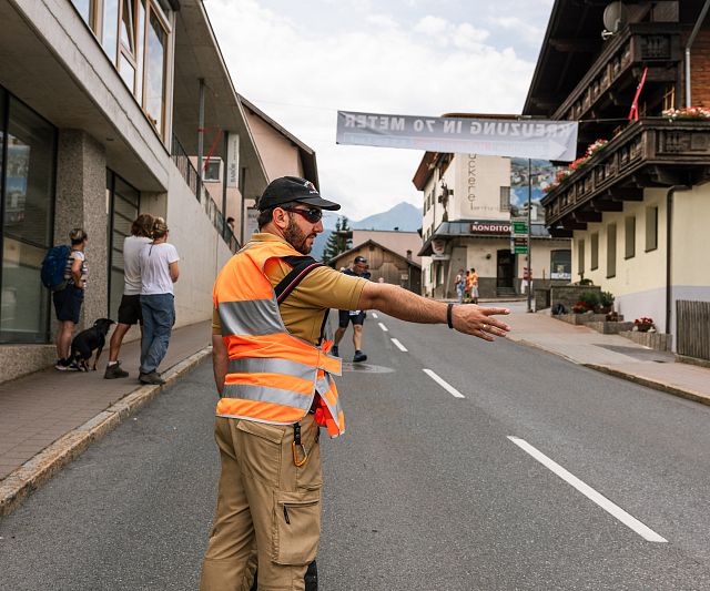Ein Feuerwehrmann steht auf der Straße und leitet den Verkehr. Im Hintergrund sind Gebäude und Menschen zu sehen.