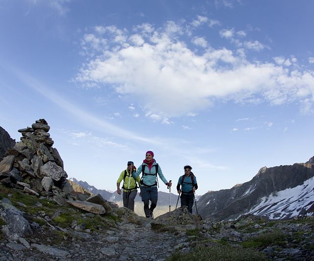 Drei Personen wandern einen felsigen Bergpfad im Pitztal, umgeben von beeindruckenden Felsen und Berglandschaften.