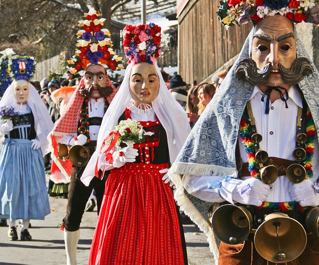 Eine Gruppe von Menschen in traditionellen Kostümen und Masken bei einem kulturellen Festumzug. Bunte Kleidung und große Hüte mit Blumen schmücken die Teilnehmer.
