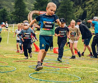 Kinder laufen begeistert durch bunte Reifen beim PKids-Wettbewerb, einer Distanz des Pitz Alpine Glacier Trails, umgeben von der beeindruckenden Alpenlandschaft.