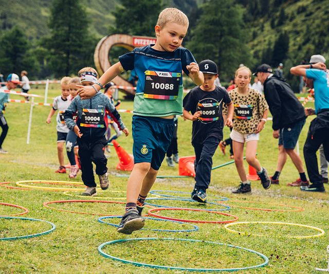 Kinder laufen begeistert durch bunte Reifen beim PKids-Wettbewerb, einer Distanz des Pitz Alpine Glacier Trails, umgeben von der beeindruckenden Alpenlandschaft.