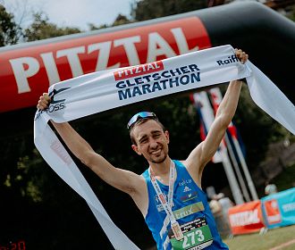 Jubelnder Marathonsieger des Gletschermarathons mit Einlaufband in den Händen.