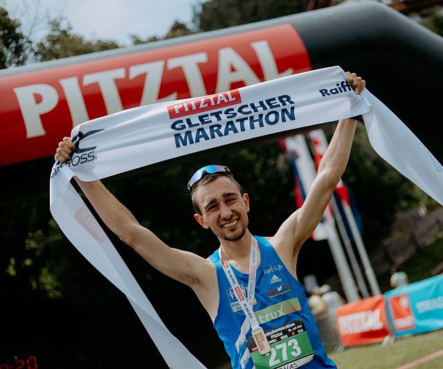 Jubelnder Marathonsieger des Gletschermarathons mit Einlaufband in den Händen.