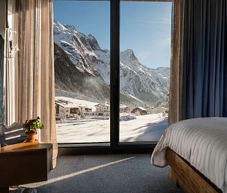 Blick aus einem Hotelzimmer mit großen Fenstern auf die verschneite Pitztaler Bergwelt.
