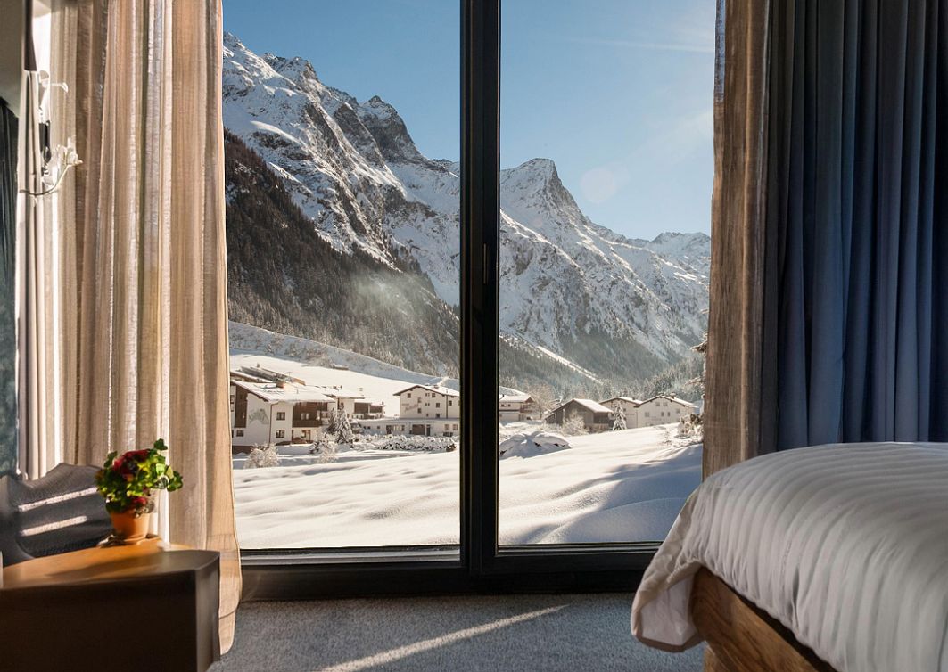 Blick aus einem Hotelzimmer mit großen Fenstern auf die verschneite Pitztaler Bergwelt.