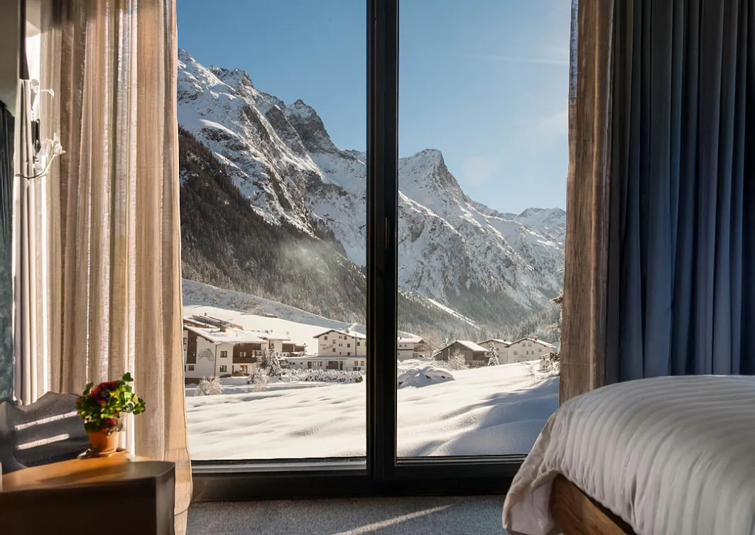 Blick aus einem Hotelzimmer mit großen Fenstern auf die verschneite Pitztaler Bergwelt.