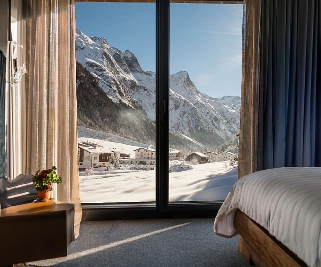 Blick aus einem Hotelzimmer mit großen Fenstern auf die verschneite Pitztaler Bergwelt.