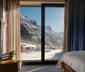 Blick aus einem Hotelzimmer mit großen Fenstern auf die verschneite Pitztaler Bergwelt.