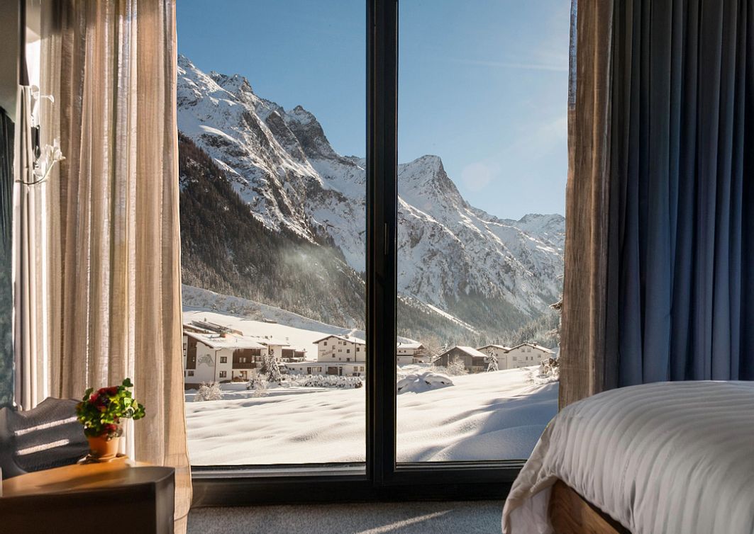 Blick aus einem Hotelzimmer mit großen Fenstern auf die verschneite Pitztaler Bergwelt.