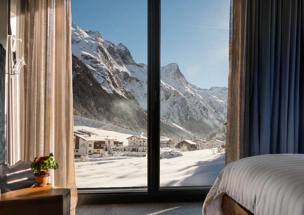 Blick aus einem Hotelzimmer mit großen Fenstern auf die verschneite Pitztaler Bergwelt.