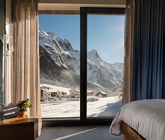 Blick aus einem Hotelzimmer mit großen Fenstern auf die verschneite Pitztaler Bergwelt.