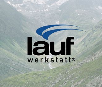 Das Bild zeigt das Logo der Laufwerkstatt auf einem unscharfen Hintergrund, der eine grüne, bergige Landschaft mit Nebel darstellt. Die Schrift ist modern und klar.